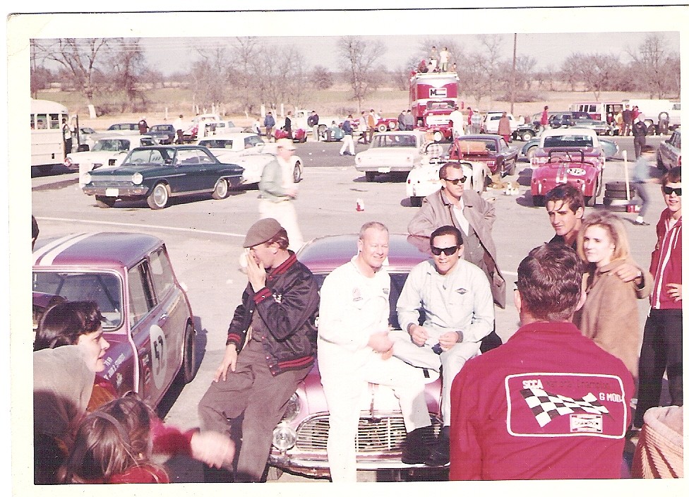 Richard McDaniel and Hugh Gammer in the paddock at Green Valley Raceway, seated on the hood of the purple Overseas Motors Mini-Cooper, surrounded by crew and spectators, circa 1966.